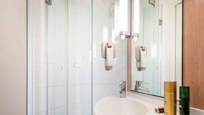 A modern bathroom with a glass shower enclosure, a white sink with a mirror, and toiletries on the sink. - ibis Paris La Villette Cité des Sciences 19ème (Paris)