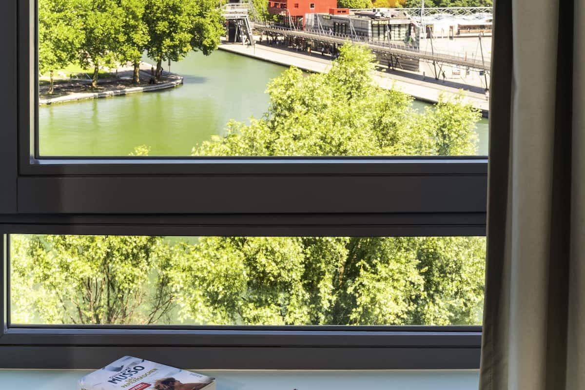 A window view of a river with a bridge, trees, and a book and glasses on a windowsill.