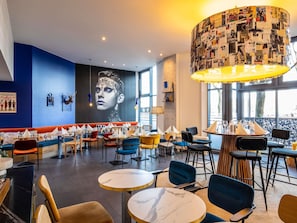 Interior moderno de restaurante con pared azul, un mural grande y diversas opciones de asientos, incluyendo mesas y cabinas.