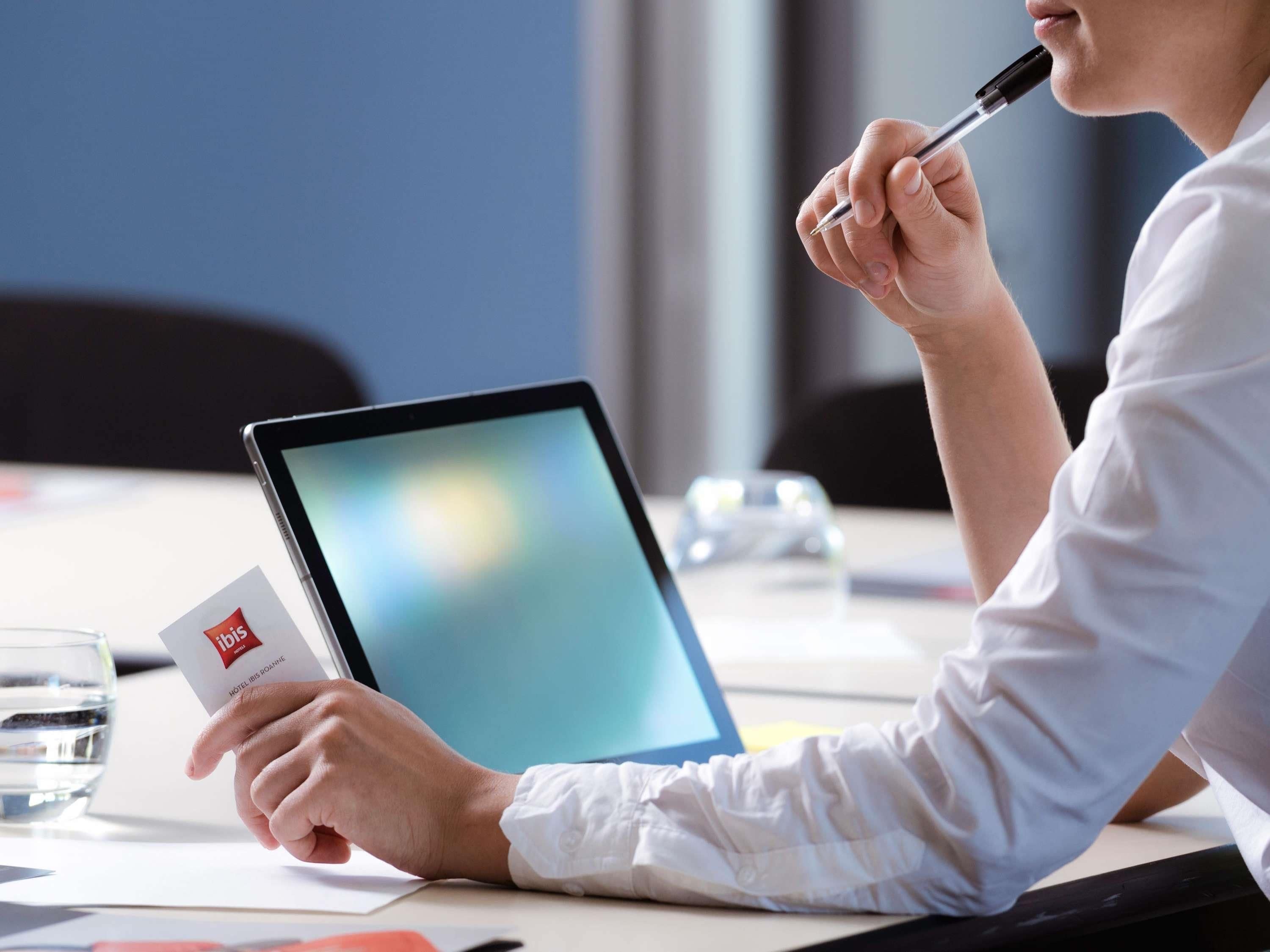 A person holding a business card and a pen, sitting at a table with a laptop in front of them.