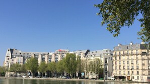 A hotel with a modern design, located beside a calm body of water, featuring a clear view of the surrounding urban landscape. - ibis Paris La Villette Cité des Sciences 19ème (Paris)