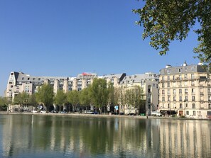A hotel with a modern design, located beside a calm body of water, featuring a clear view of the surrounding urban landscape. - ibis Paris La Villette Cité des Sciences 19ème (Paris)