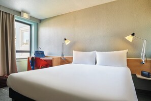 Habitación de hotel con una cama grande, dos lámparas de noche, un escritorio con una silla, un bolso y una ventana con cortinas.