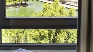 Une vue par la fenêtre sur une rivière, un pont, des arbres, ainsi qu’un livre et des lunettes posés sur un rebord de fenêtre.