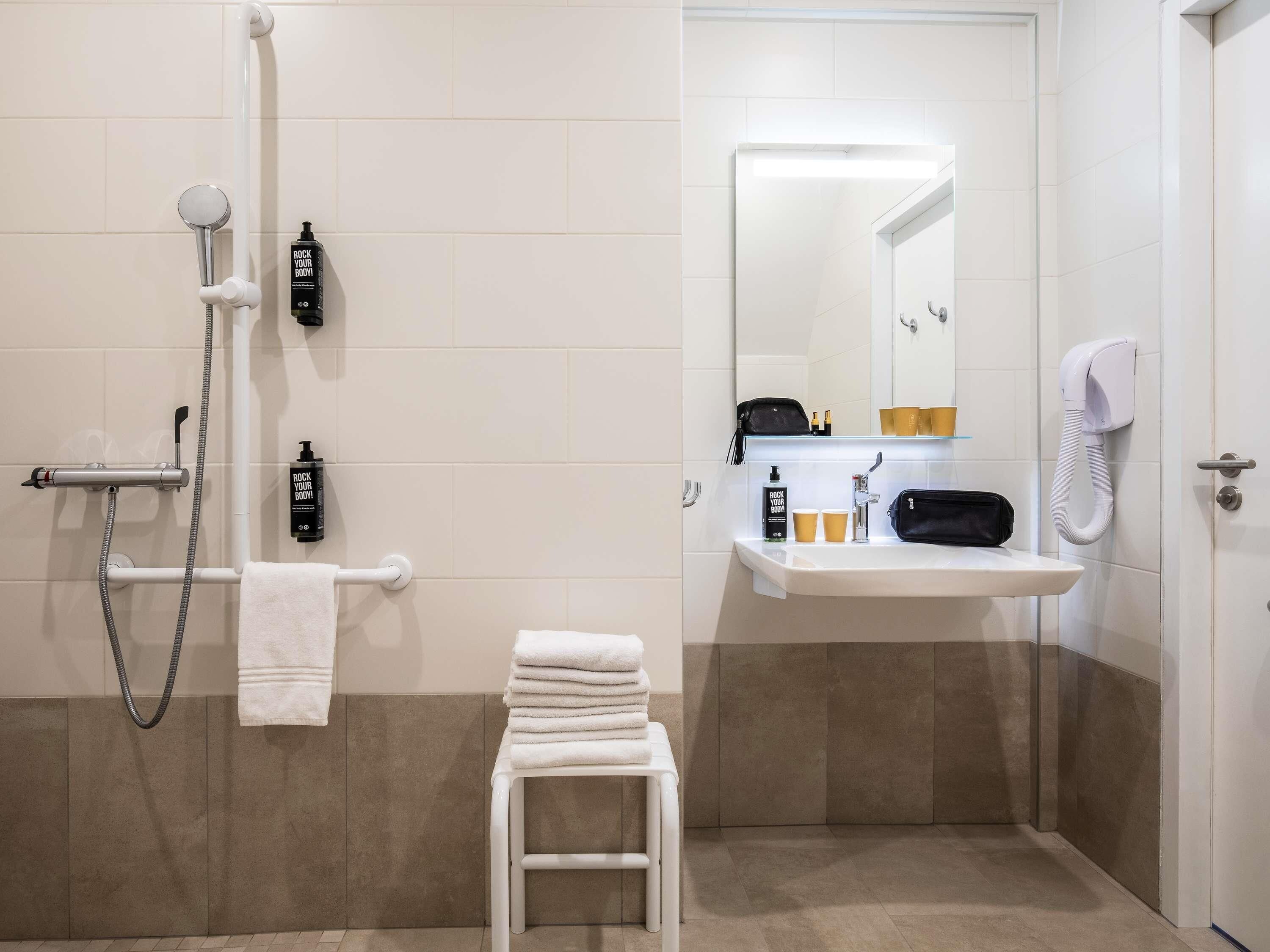 A bathroom with a shower, a sink, a mirror, and a towel rack.