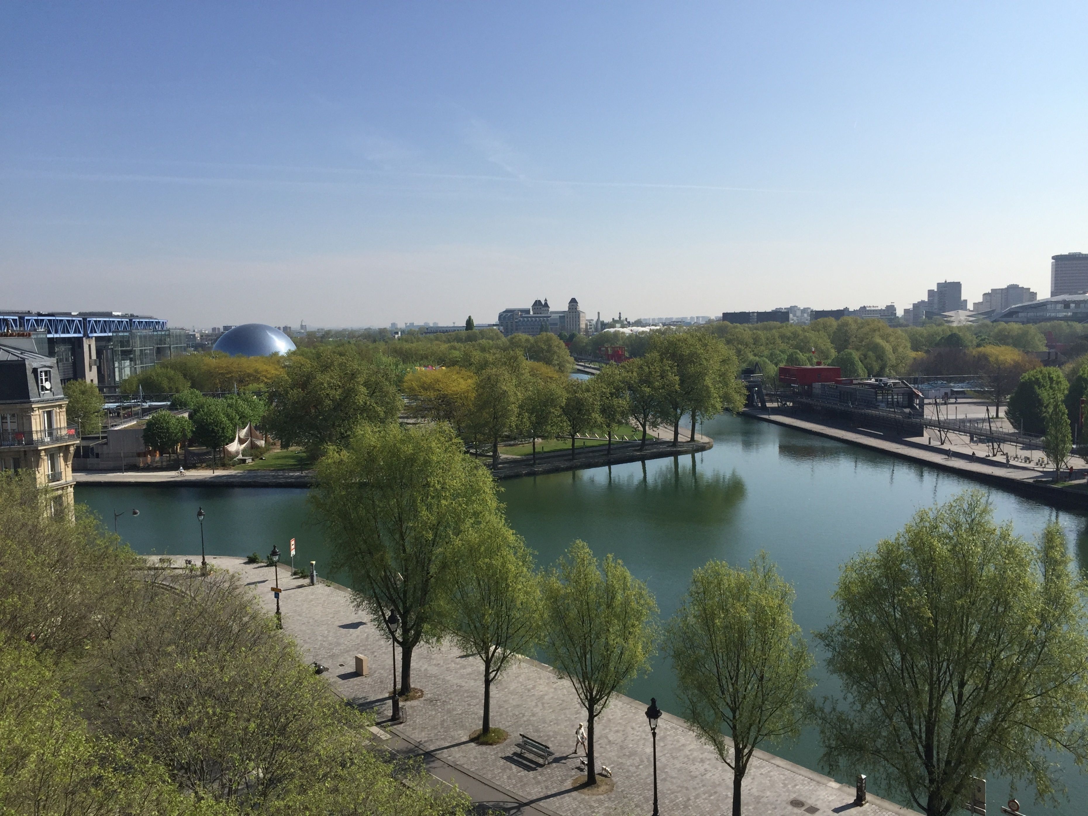 A riverside view with trees, a bridge, and buildings in the background.