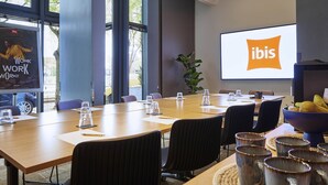 A conference room with a large screen displaying the ibis logo, a long table with chairs, and a plant. - ibis Paris La Villette Cité des Sciences 19ème (Paris)