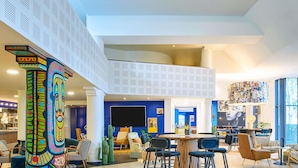 A spacious lobby with a high ceiling, a central seating area, and a large TV screen. - ibis Paris La Villette Cité des Sciences 19ème (Paris)