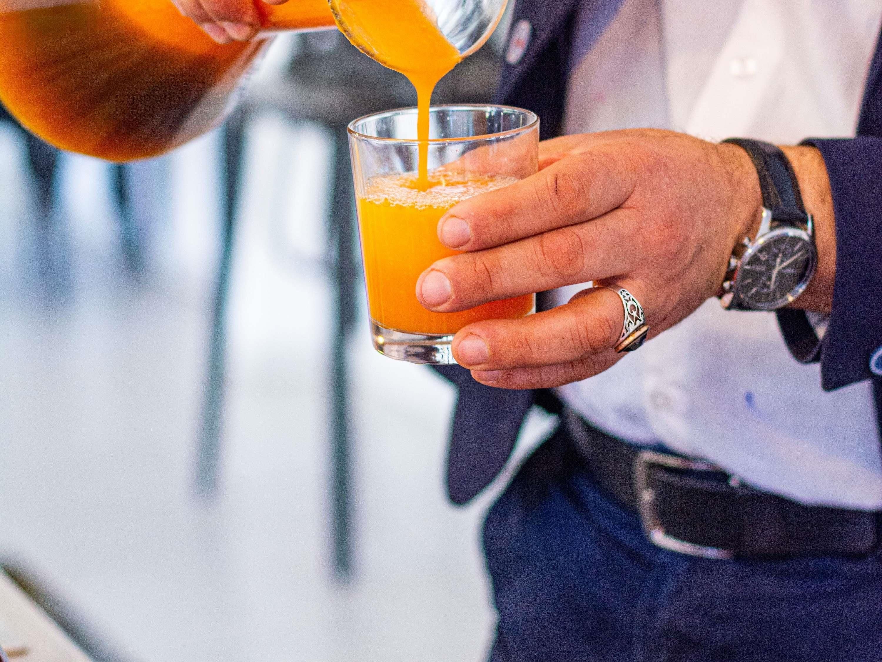 Une personne verse un liquide orange dans un verre transparent.