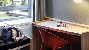 A modern room with a desk, chair, and a view of a body of water through a window. - ibis Paris La Villette Cité des Sciences 19ème (Paris)