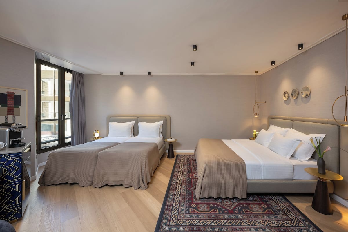 Moderni hotellihuone, jossa on kaksi sänkyä, suuri ikkuna, kahvinkeitin ja koristeellinen matto.