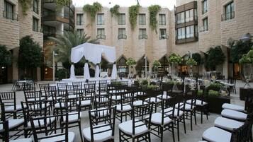 Un patio con hileras de sillas dispuestas para un evento, rodeado de edificios con balcones y vegetación.