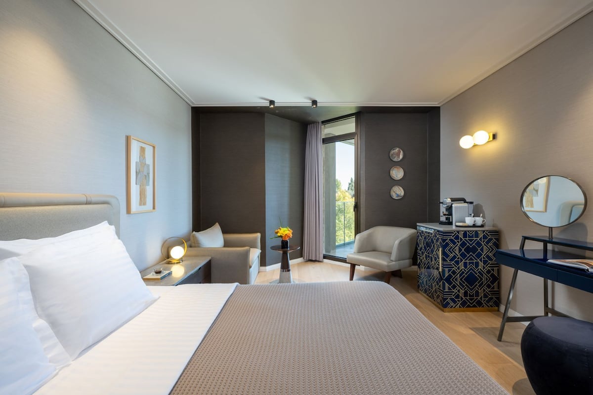 Moderni hotellihuone, jossa on sänky, sohva, peilillä varustettu työpöytä ja näkymä ulos.