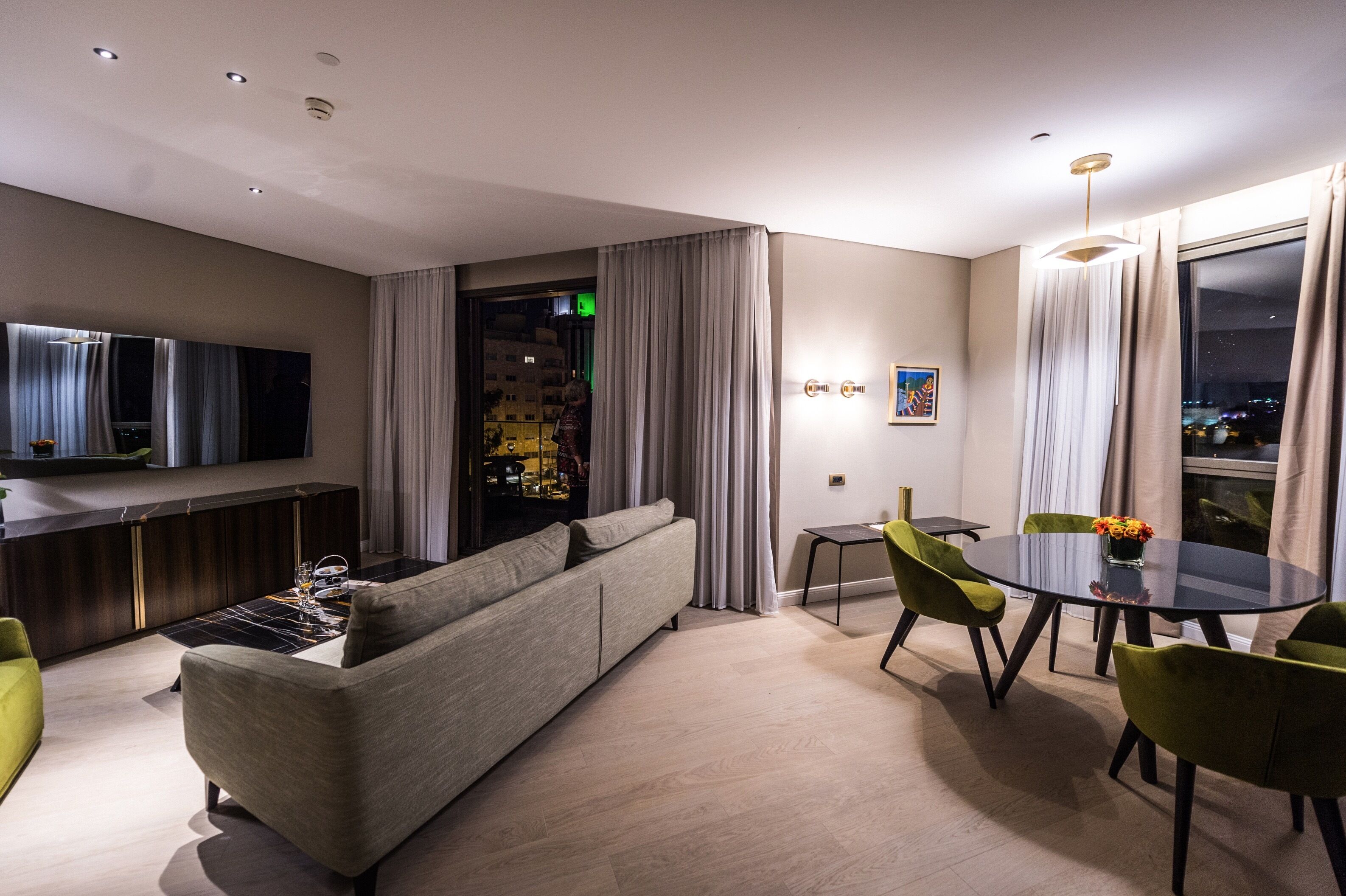 Ein modernes Wohnzimmer mit Sofa, Esstisch, Stühlen, einem Flachbildfernseher und einem großen Fenster mit Vorhängen.