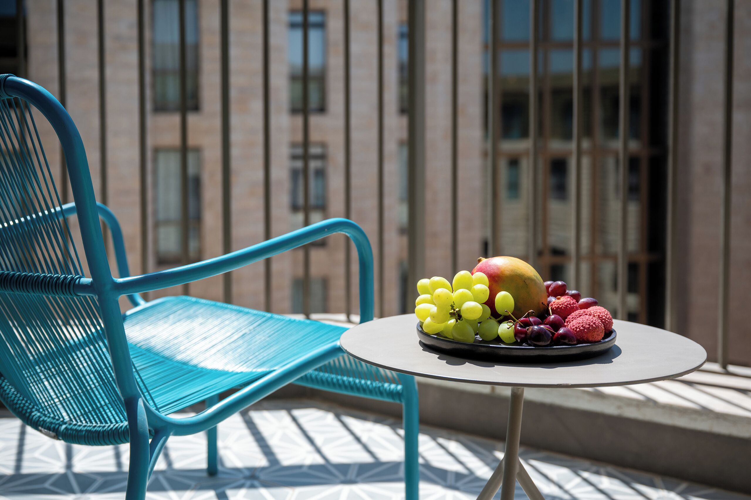 A blue chair and a table with a fruit platter on a balcony with a building in the background.