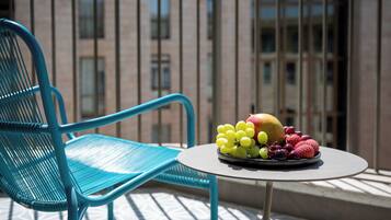 A blue chair and a table with a fruit platter on a balcony with a building in the background.