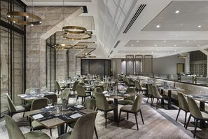 A modern restaurant with high ceilings, stone walls, and multiple dining tables with chairs.