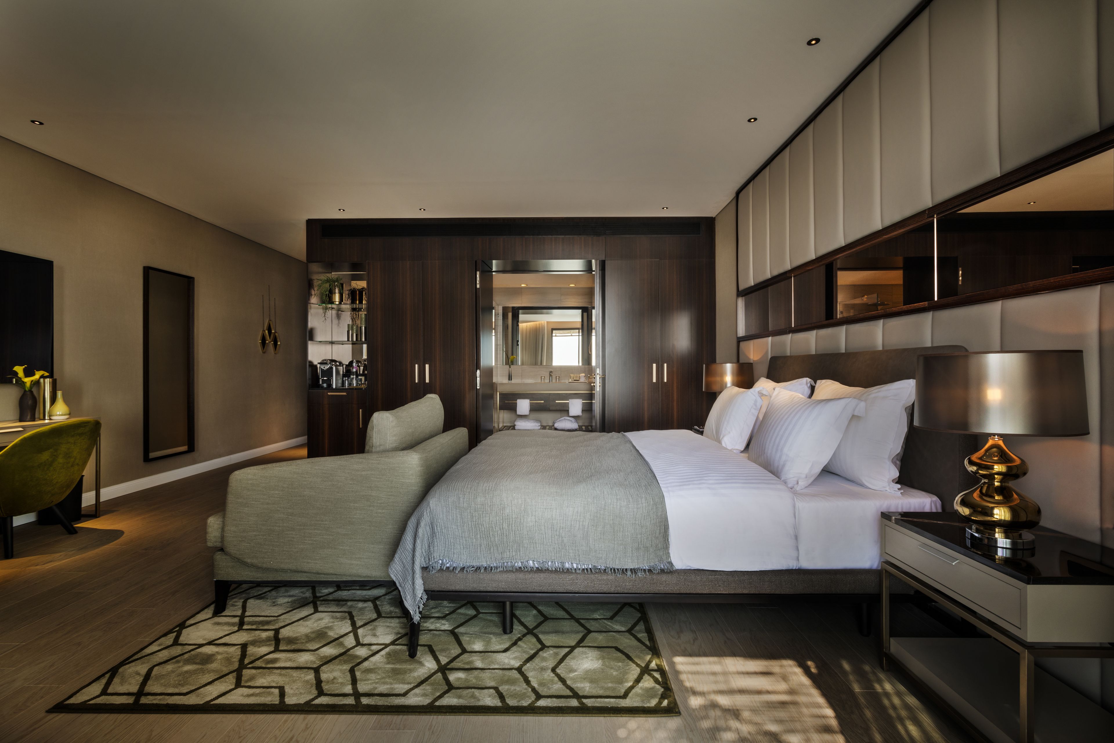 Une chambre d’hôtel moderne dotée d’un grand lit, d’un coin salon avec un canapé, d’un bureau avec une lampe et d’un grand miroir.