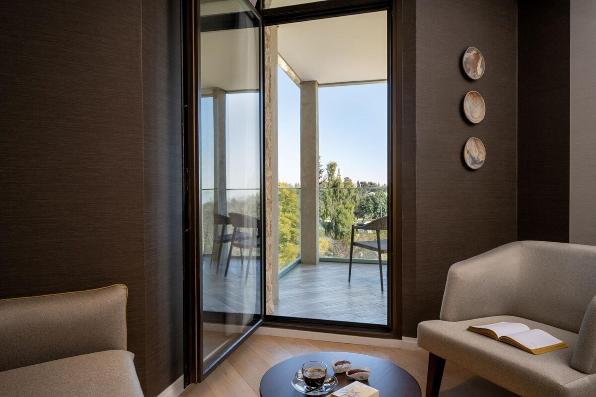 Une chambre moderne avec une grande fenêtre, une table ronde sur laquelle se trouvent un livre et une tasse, ainsi qu’une chaise.