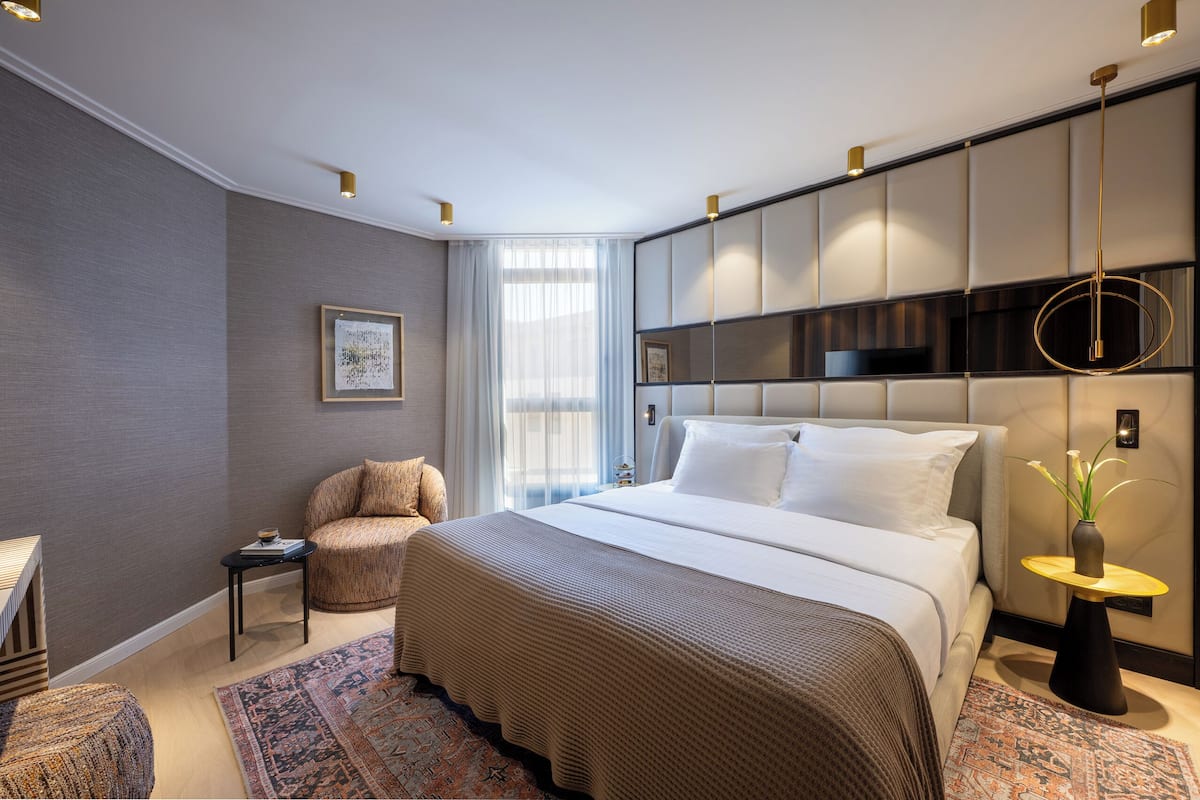 Moderni hotellihuone, jossa on suuri sänky, oleskelualue, jossa on tuoli ja pieni pöytä, sekä koristeellinen maljakko.