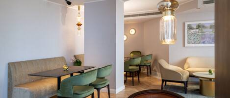 A modern dining area with a wooden table, green upholstered chairs, a beige sofa, and a round coffee table.