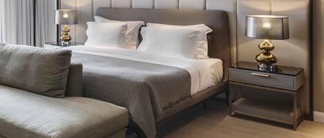 A modern hotel room with a large bed, two bedside tables with lamps, a sofa, and a decorative mirror above the bed.