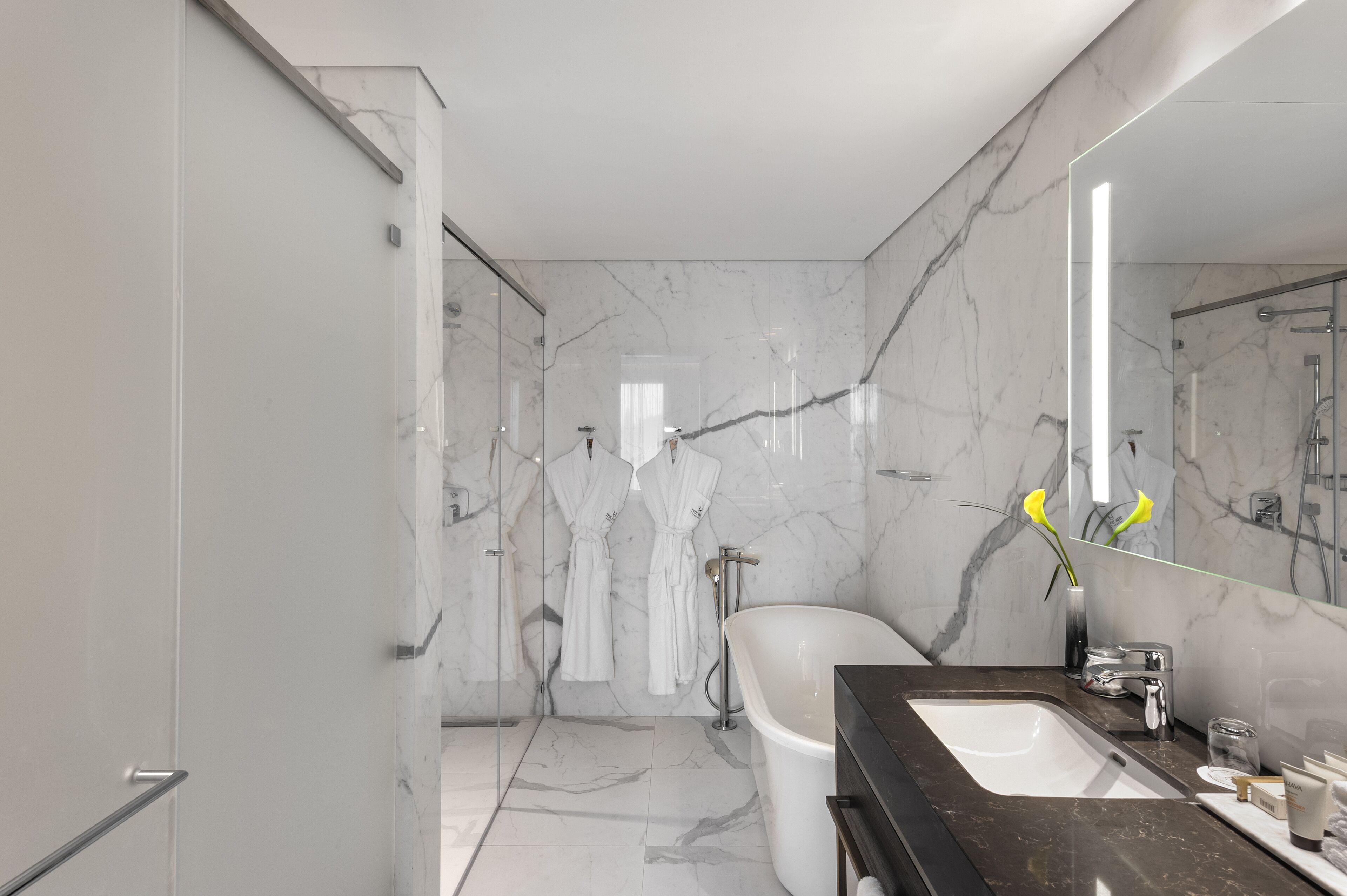 A modern bathroom with a marble floor, a freestanding bathtub, a vanity with a dark countertop, and a large mirror.