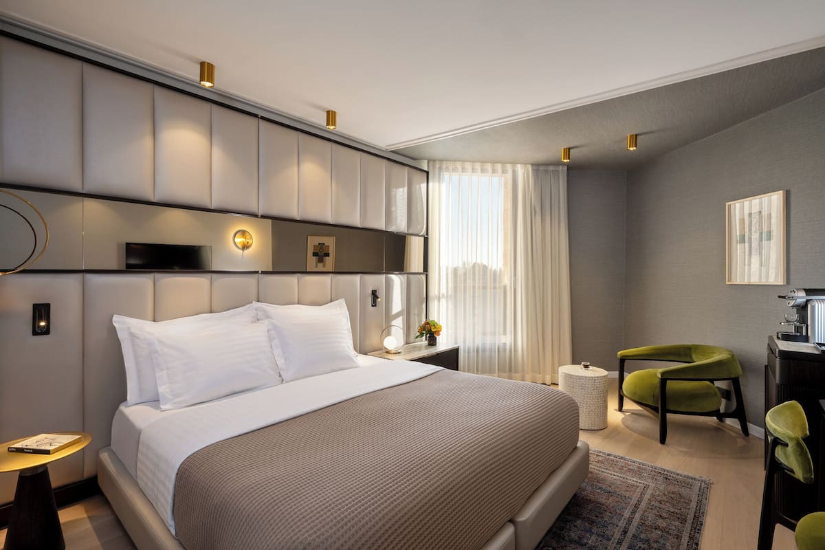 Moderni hotellihuone, jossa on suuri sänky, työpöytä, tuoli ja pieni pyöreä pöytä.