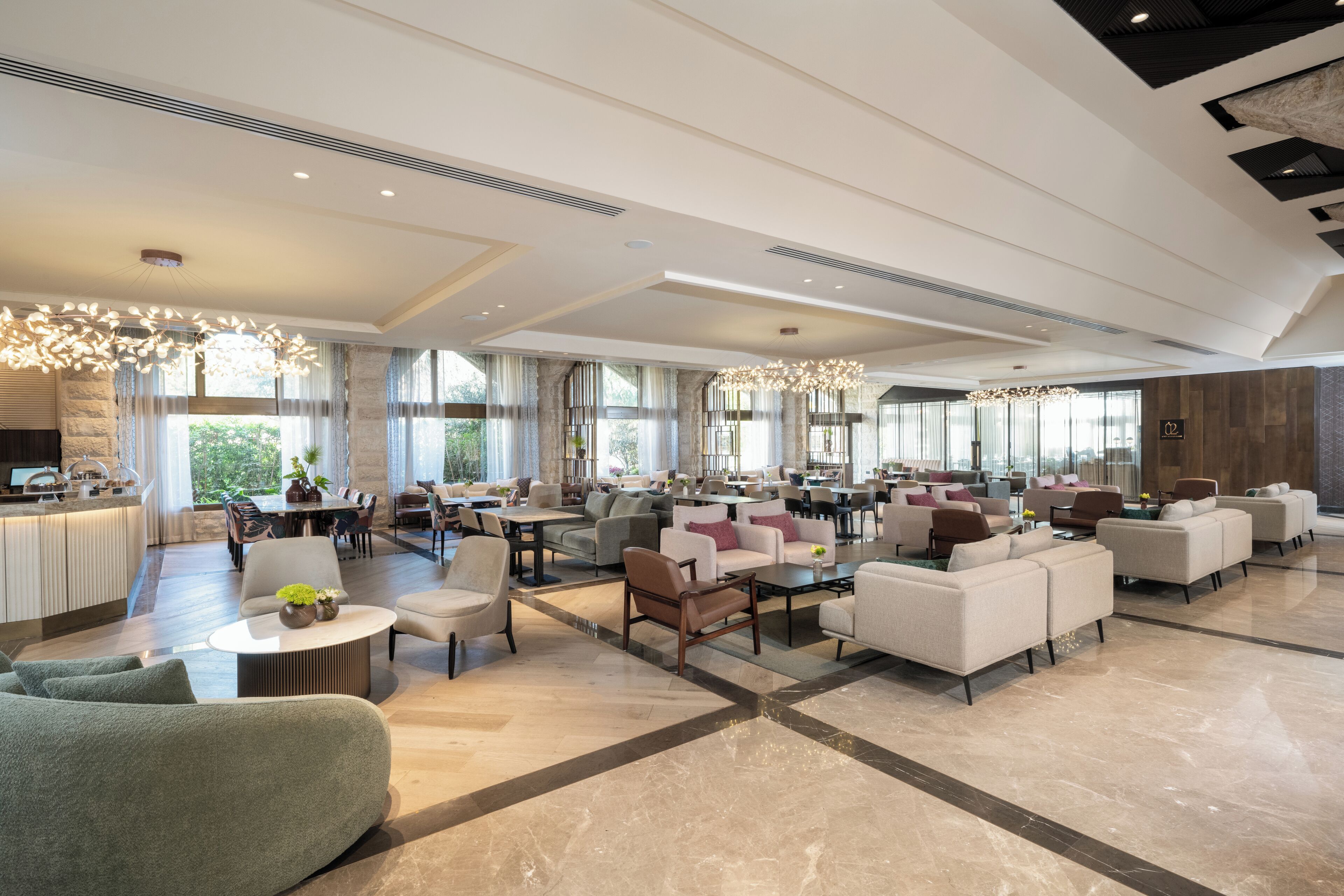 Un amplio vestíbulo de hotel con varias zonas de estar, una recepción y grandes ventanales que ofrecen luz natural.