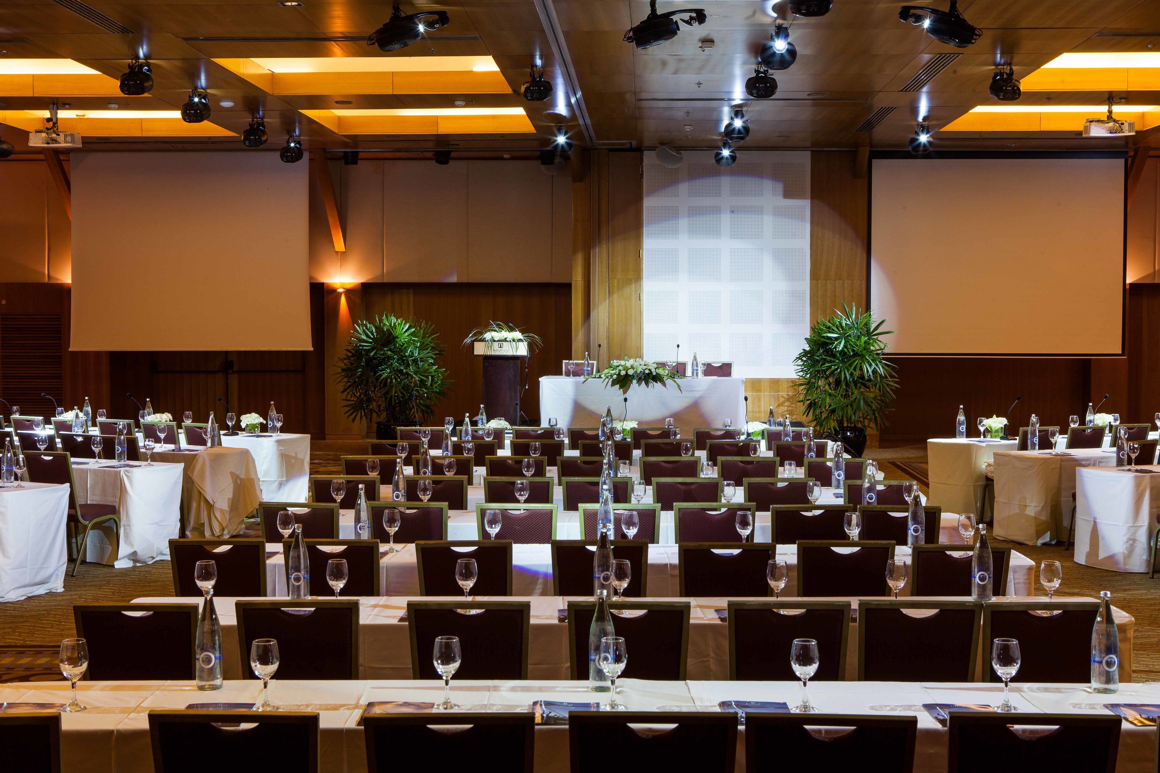 A banquet hall with rows of tables set for dining, each with wine glasses and water bottles.
