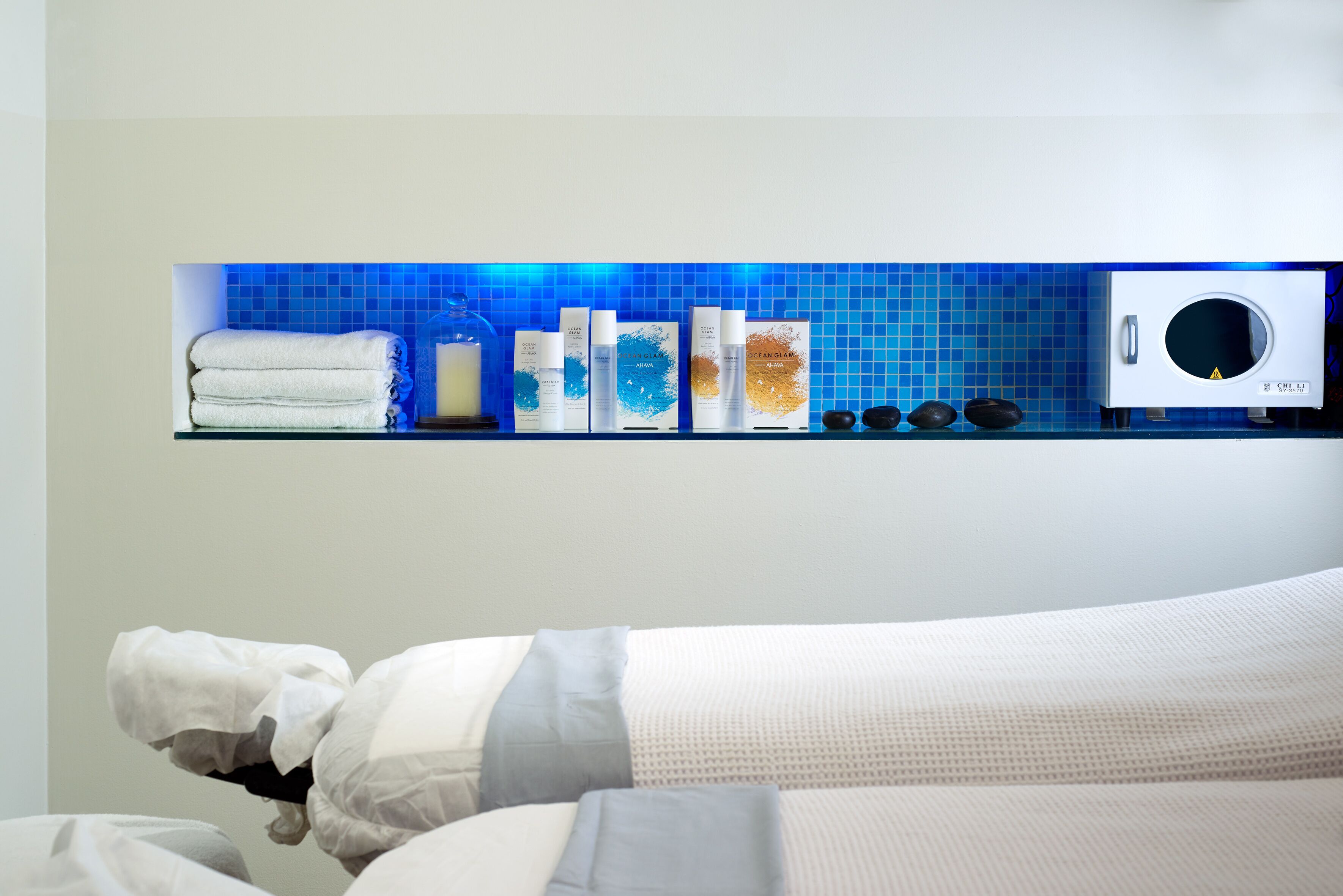 A bathroom with a blue-tiled wall, a glass shelf with toiletries, a white towel, and a white washing machine.