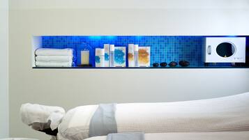 Un baño con pared de azulejos azules, un estante de vidrio con artículos de tocador, una toalla blanca y una lavadora blanca.