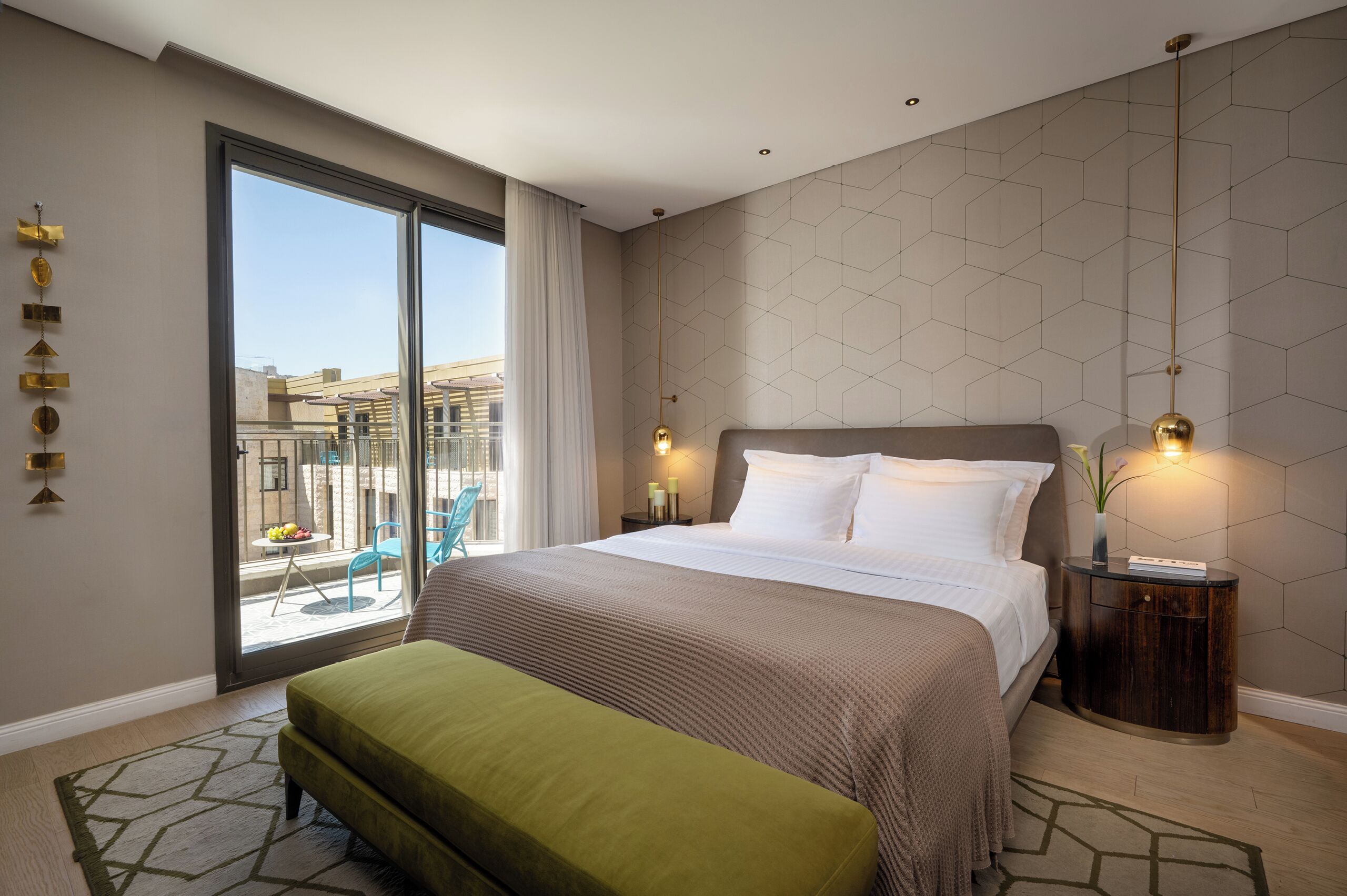 Une chambre d’hôtel moderne dotée d’un grand lit, d’une banquette, d’une table de chevet avec des lampes et offrant une vue sur la ville grâce à une grande fenêtre.