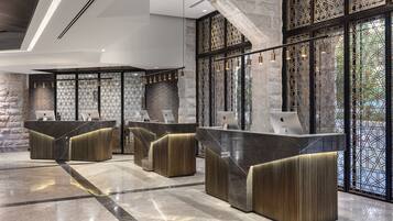 A modern reception area with three counters, each with a laptop and a chair. The area features a stone wall and large windows with a geometric pattern.