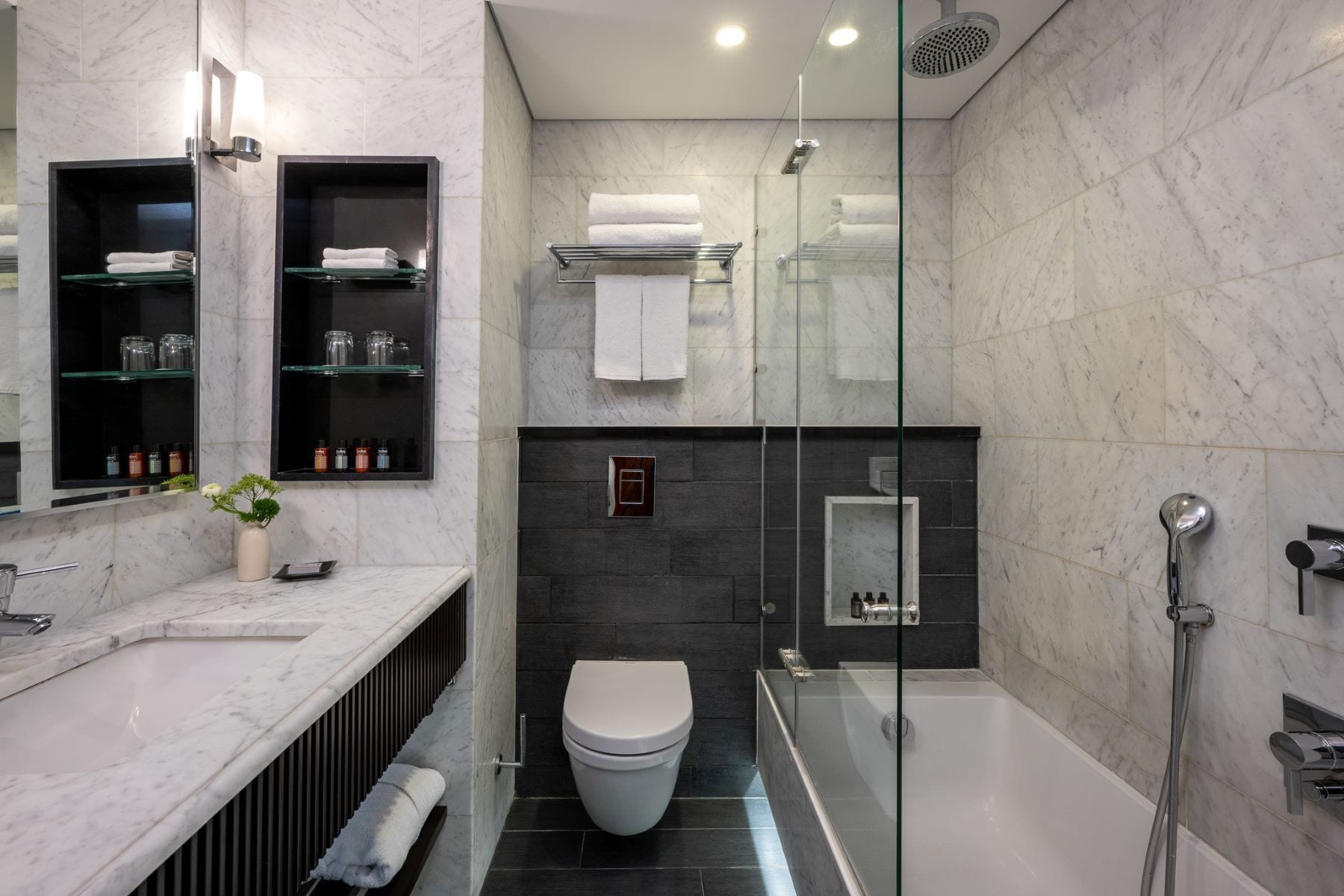 Une salle de bain moderne dotée d’une douche à parois de verre, de toilettes blanches et d’un lavabo dont le plan est recouvert de carreaux de marbre.