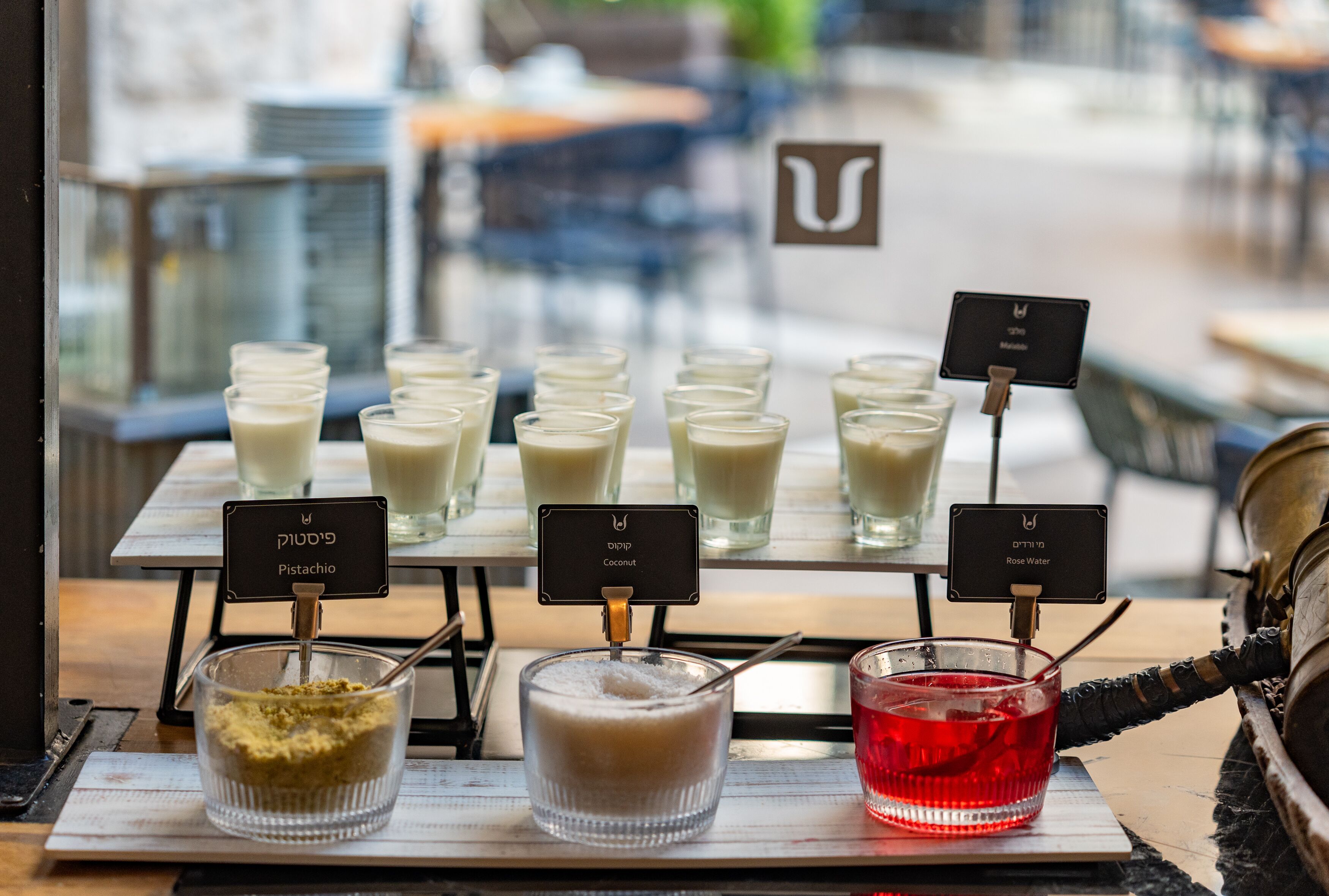 A beverage station with various drinks and a sign indicating 'Pistachio' and 'Coconut' flavors.