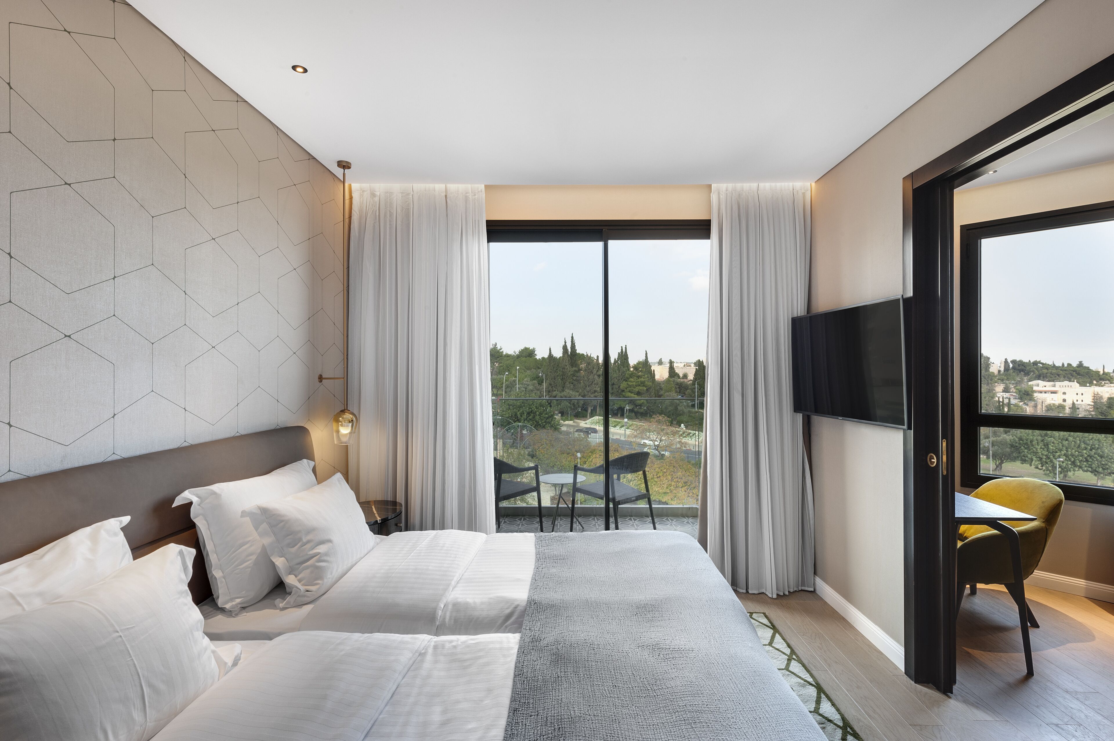A hotel room with a large bed, a TV, a balcony with a view, and a table with chairs.