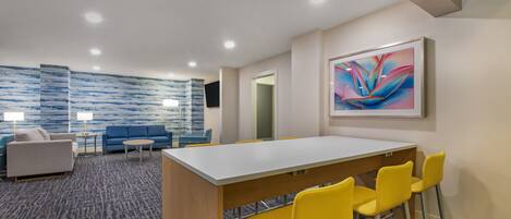 A modern hotel room with a large desk, yellow chairs, a sofa, and a blue accent wall.