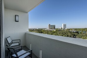 A balcony with two chairs and a table, overlooking a cityscape with buildings and greenery.