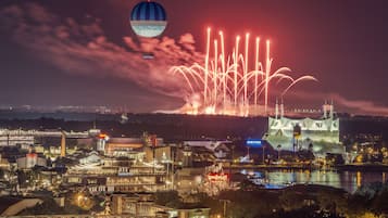 A nighttime cityscape with fireworks, a hot air balloon, and a large water tower structure.
