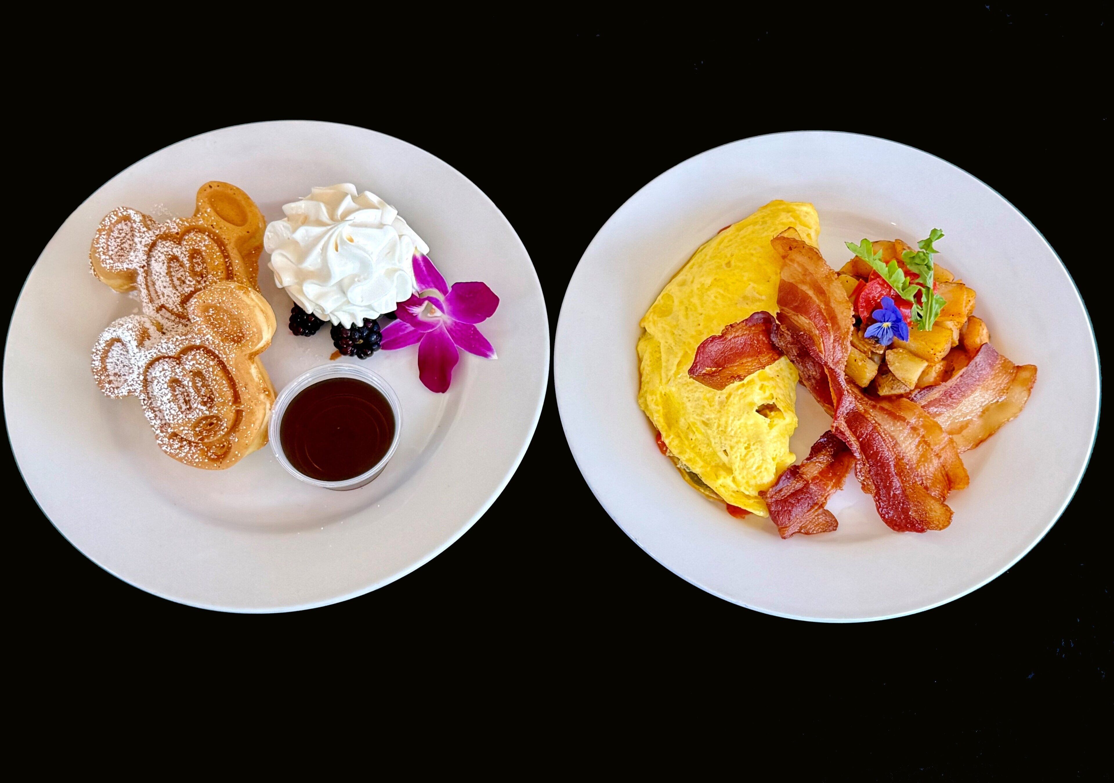 Two plates of breakfast food, one with waffles and the other with eggs and bacon.