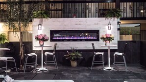 A modern outdoor seating area with a fireplace, two tables with chairs, and potted plants. - Best Western Plus Cairn Croft Hotel (Niagara Falls)