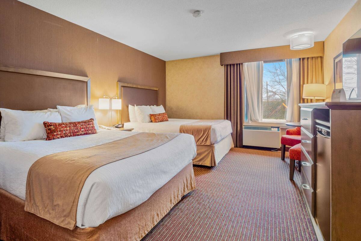 A hotel room with two beds, a desk, a chair, and a window with curtains.