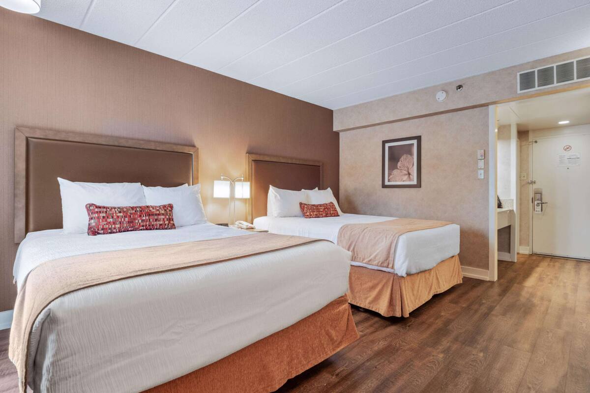 A hotel room with two beds, a wooden floor, a door with a sign, and a wall-mounted light fixture.