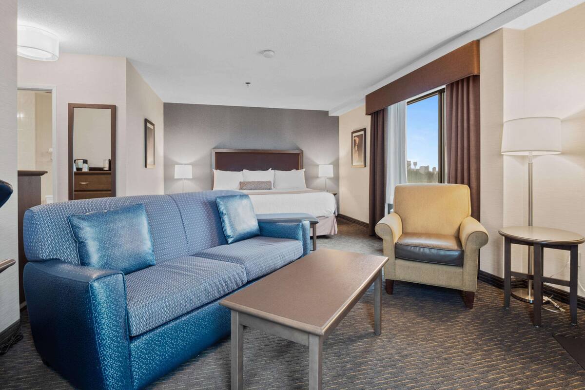 A hotel room with a bed, a blue sofa, a small table, a chair, and a lamp.