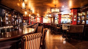 A bar area with wooden flooring, striped cushioned seating, and a bar counter with a cash register. - Best Western Plus Cairn Croft Hotel (Niagara Falls)