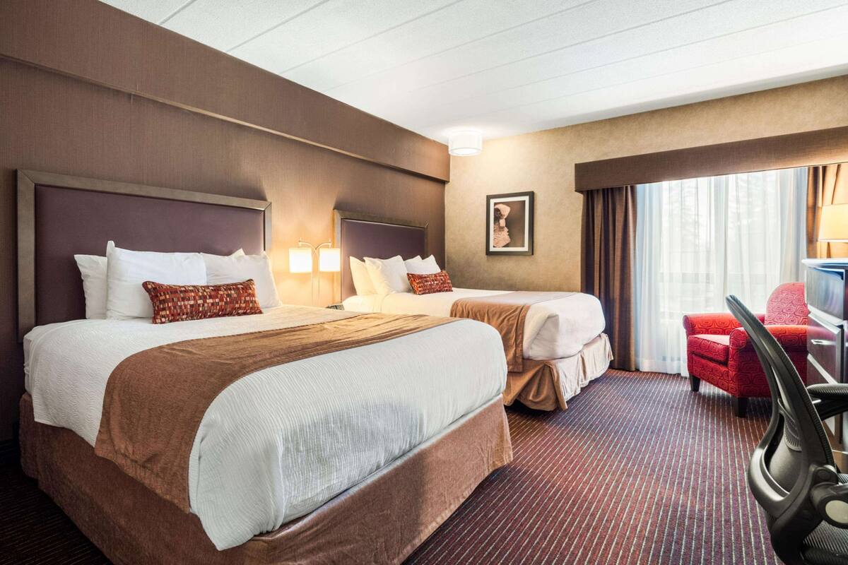 A hotel room with two beds, a desk, a chair, and a large window with curtains.