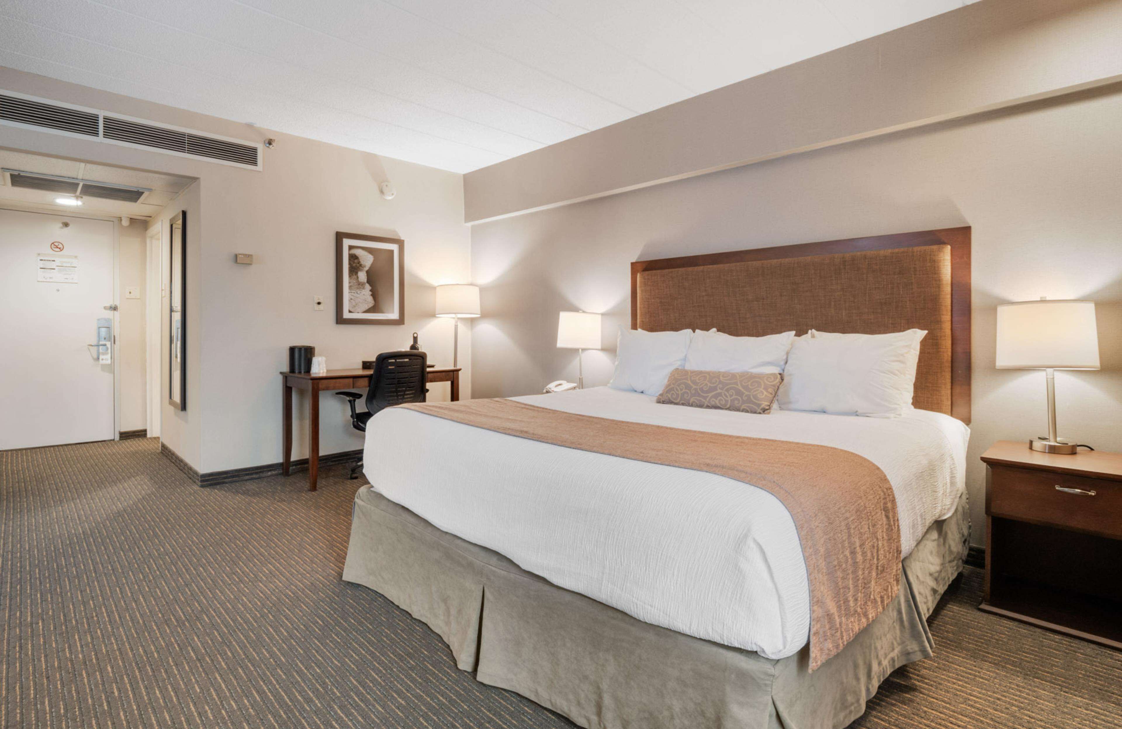 A hotel room with a large bed, bedside lamps, a desk with a chair, and a framed picture on the wall.