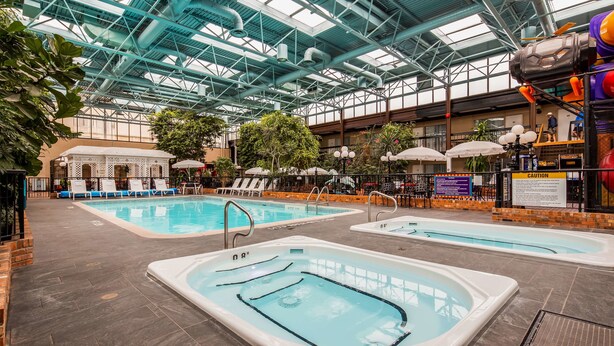 An indoor swimming pool area with two pools, lounge chairs, and a covered seating area. - Best Western Plus Cairn Croft Hotel (Niagara Falls)