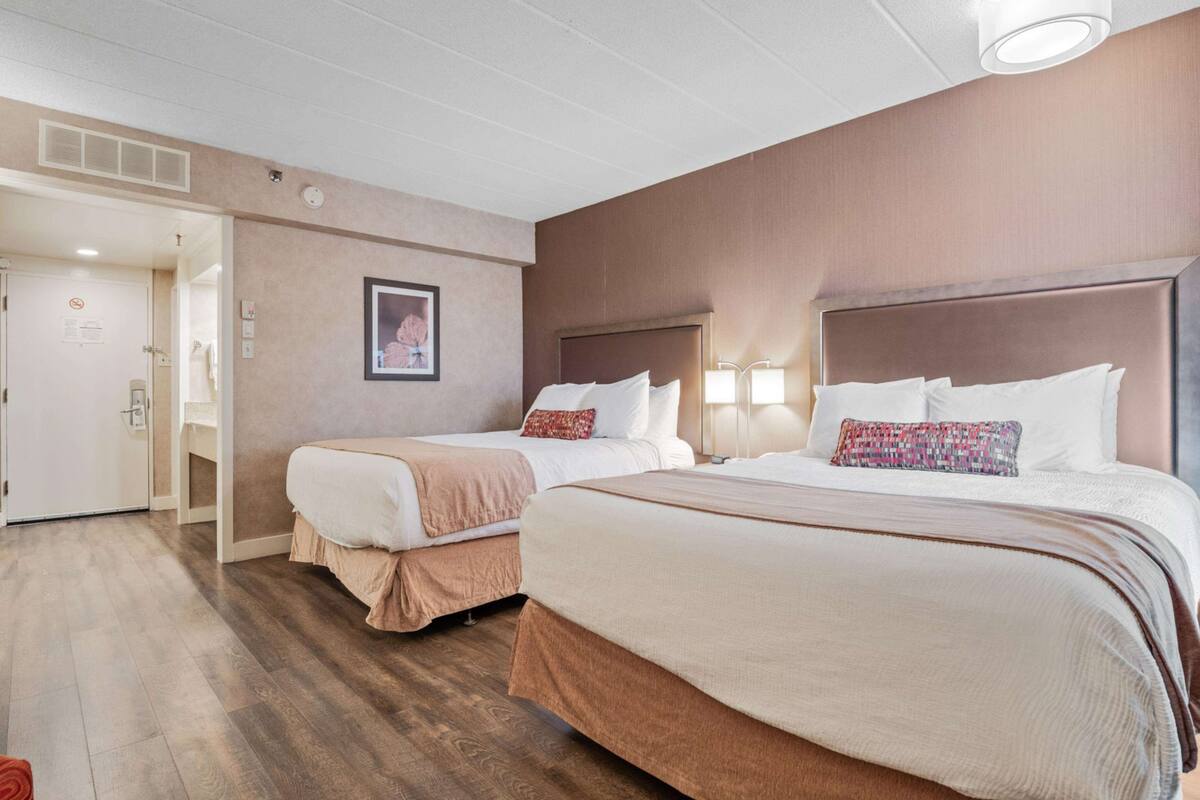 A hotel room with two beds, a door leading to a bathroom, and a framed picture on the wall.